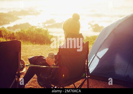 Sweet solitude as the sun rises. Rear view of a young woman sitting in a camping chair and enjoying the scenery. Stock Photo
