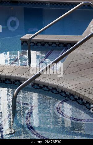 Pool surface reflecting city high rise. Stairs and handrail leading into crystal clear water Stock Photo