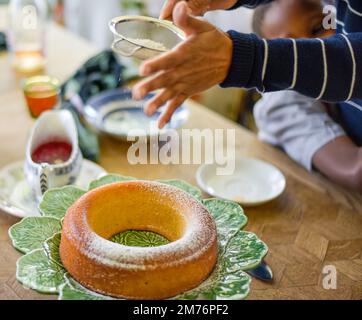 Woman Dusting the top of a moist round sponge cake with fine sifted powdered sugar Stock Photo