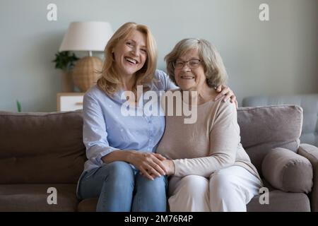 Positive adult daughter woman and elderly mother sitting on sofa Stock Photo