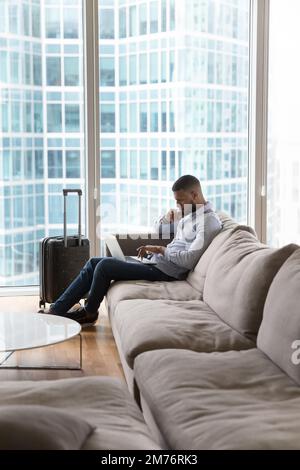 Serious pensive African businessman sit on sofa working on laptop Stock Photo