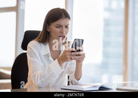 Young female staring at smart phone screen read awful sms Stock Photo