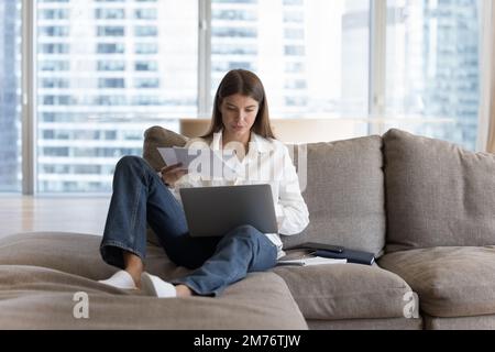 Busy woman sitting on sofa working or studying use laptop Stock Photo