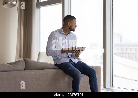 African man holds digital tablet looking out window to city Stock Photo