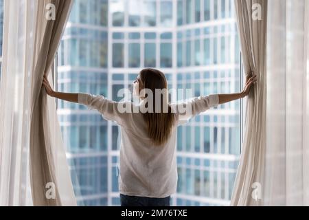 Woman opens curtains looking out window of luxury modern apartment Stock Photo