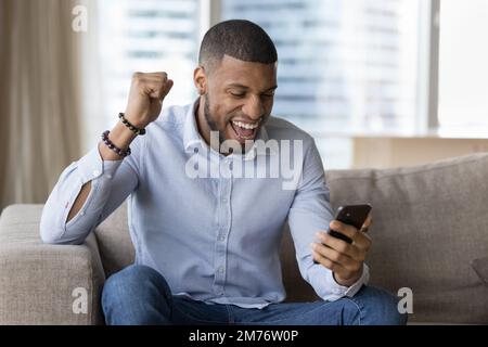 Happy African guy holds smartphone celebrates great news Stock Photo