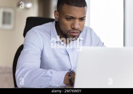 Focused African businessman working at workplace using laptop Stock Photo