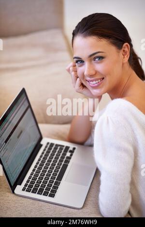 Hows this smile for my profile update. a young woman sitting in her living room using a laptop. Stock Photo