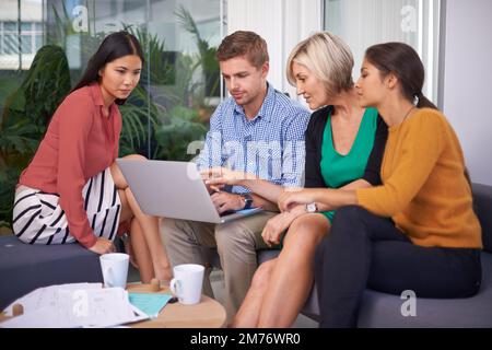 A successful team is a group of many hands and one mind. A team of coworkers sitting and working on a laptop together. Stock Photo