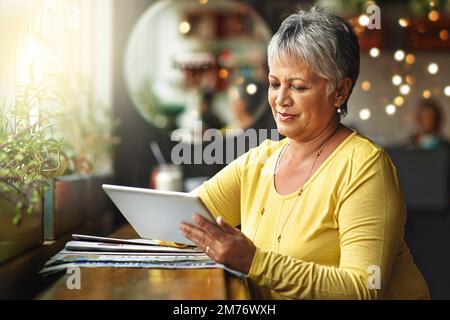 I go where the wifi is. a mature woman using a digital tablet in a coffee shop. Stock Photo