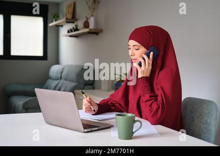 Muslim young woman student in hijab in a phone call while studying at home. Stock Photo