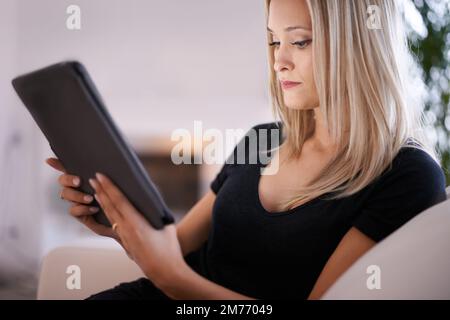 Doing some deep reading. a young blonde woman relaxing at home with her digital tablet. Stock Photo