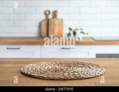 Wooden oak countertop with napkin and free space for mounting a product or layout against the background of a blurred white kitchen with plant. Horizo Stock Photo