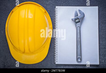 Notebook building helmet adjustable wrench on black background construction concept. Stock Photo