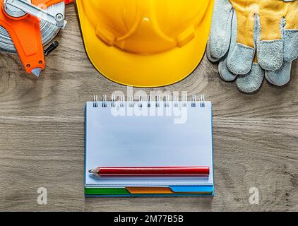 Notepad pencil safety gloves tape measure hard hat on wooden board. Stock Photo