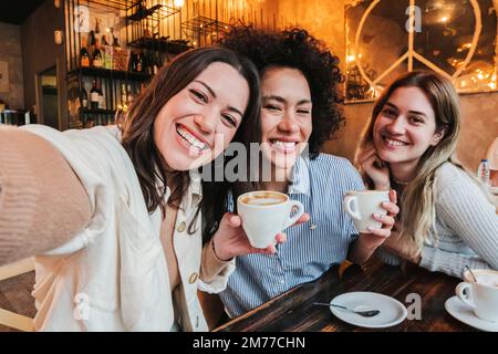 Group of three happy young women taking a selfie portrait on a coffee shop. Multi ethnic friends taking a photo smiling and looking at camera. High quality photo Stock Photo