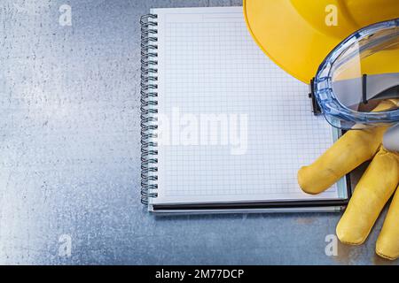Protective spectacles gloves copybook hard hat on scratched metallic background. Stock Photo