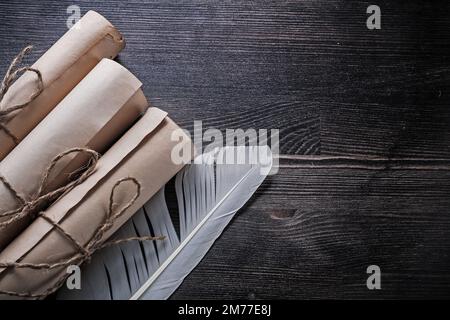 Rolled up vintage papers with feather on wooden board. Stock Photo
