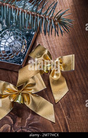 two golden christmas bows with little bells and mirror disco balls and pinetree branch on old wooden board Stock Photo