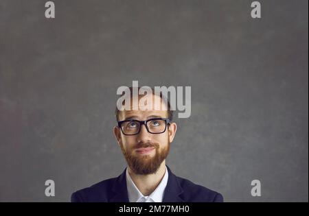 Portrait of unsure male employee with funny dreamy facial expression on gray background. Stock Photo