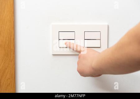 Close up of female finger is turn on or off on light switch with white wall at home copy space. Stock Photo