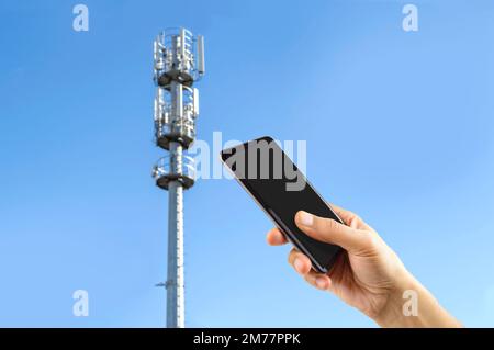 Closeup of hand using phone phone tower cellular sky background. Stock Photo