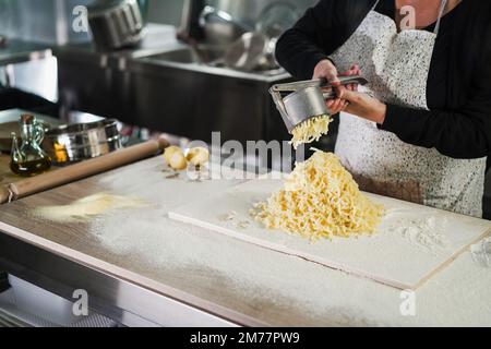 Woman using potato press for fresh hand made gnocchi inside pasta factory Stock Photo