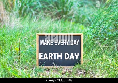 Close up of a chalkboard with the text make every day earth day written in it, on the ground in the woods Stock Photo