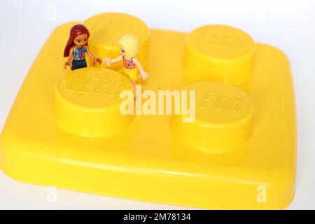 2 Lego girls figure holding hands standing on a large yellow block Stock Photo