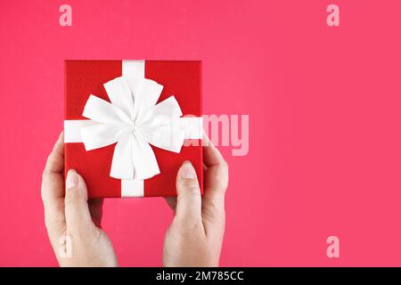 Red box with a bow in female hands. Gift on a pink background. Holidays concept birthday, Christmas, Valentine's day. Copy space Stock Photo
