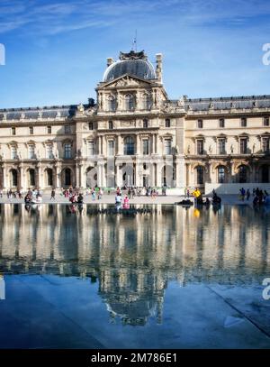 Tourists mill around the Louvre inner courtyard where the historic building reflects in one of its outdoor pools in Paris, France. Stock Photo
