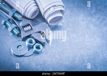 Adjustable spanner bolt washers construction nuts screwbolts and rolled up blueprints on scratched metallic background maintenance concept. Stock Photo