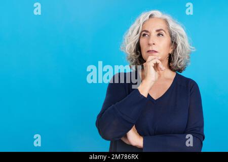 Mature woman gesturing and looking up with pensive expression Stock Photo