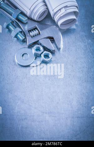 Adjustable spanner bolt washers nuts bolts and rolled up construction drawings on metallic background maintenance concept. Stock Photo