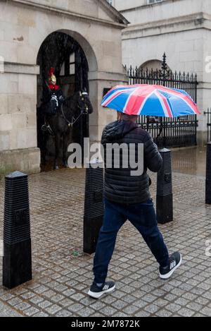 Whitehall, Westminster, London, UK. 8th Jan, 2023. Heavy rain has hit the tourist areas of Westminster with a few people out on the streets. Mounted guard at Horse Guards with person passing with umbrella Stock Photo