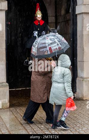 Whitehall, Westminster, London, UK. 8th Jan, 2023. Heavy rain has hit the tourist areas of Westminster with a few people out on the streets. Mounted guard at Horse Guards with person passing with London tourist umbrella Stock Photo