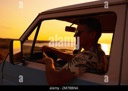 Horizontal photo of a caucasian man driving a camper van during sunset Stock Photo