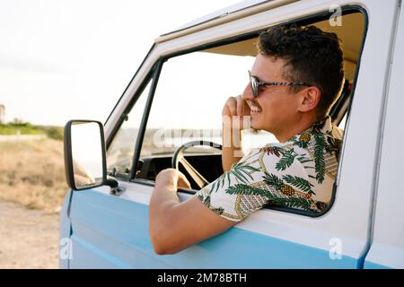 Rear view of a happy man talking to the mobile while driving a camper van Stock Photo