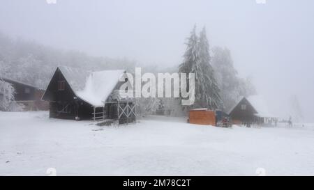 Fantastic winter landscape with glowing wooden house against the backdrop of glowing city lights in fog. Cozy cabin in Carpathian mountains. Christmas Stock Photo