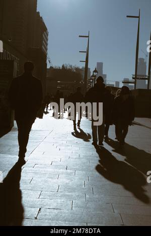 Silhouette Of A Crowd Of People Walking ALong The South Bank By Westminster Bridge Backlit By The Sun In Winter, London UK Stock Photo