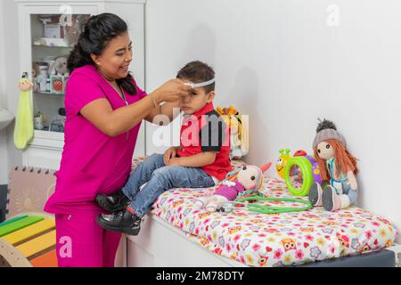 Pediatrician doctor measuring the head of a child who is sitting on the table in her office. Stock Photo