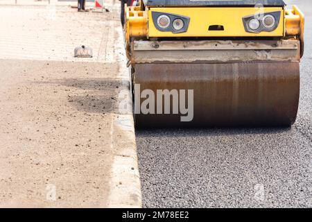 The wheel of a large road roller rams and compacts the new asphalt on the road lane. Close-up. Copy space. Stock Photo