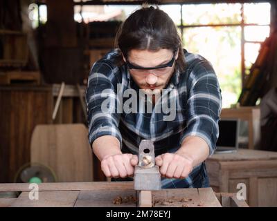 The carpenter using a manual plane for woodworking in his workshop Stock Photo