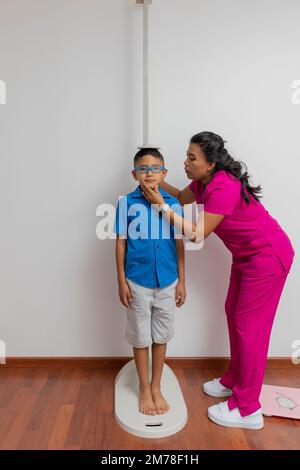Latina pediatrician measuring a child with a wall ruler in her office. Stock Photo