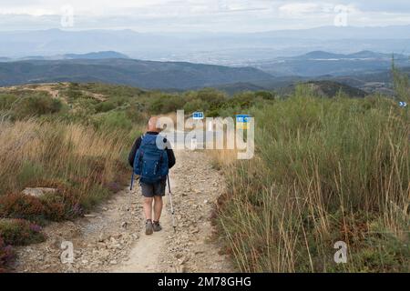 A pilgrim on the Camino Frances approaches the E-142 road near the village of El Acebo in León, Spain. In the distance is the city of Ponferrada. This Stock Photo