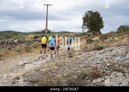 A group of pilgrims pass a stone arrow on the trail marking the way along the Camino Frances near the village of Foncebadón in León, Spain. This ancie Stock Photo