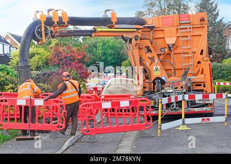 Suction excavator hgv lorry truck & driver back view one hand on remote control working beside gas main contractor exposing house gas connection UK Stock Photo