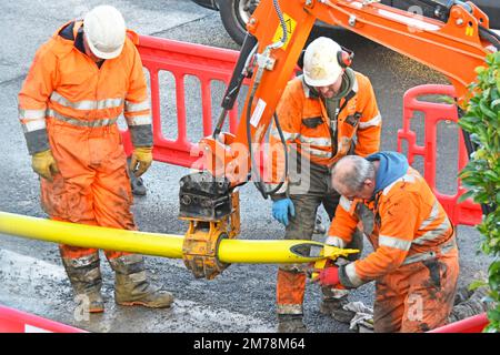 Three man gas main insertion team wait for point to be cut one end of coiled 125mm yellow plastic replacement tube for insertion in old steel pipe UK Stock Photo