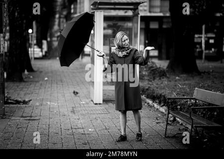 A woman opens her umbrella outside checking for rain. Black and white photo. Stock Photo