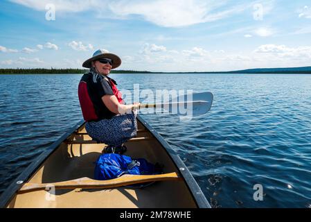 Senior female tourist paddles a canoe across Deadman Lake; Deadman Lake Campground; Tetlin National Wildlife Refuge; Alaska; USA